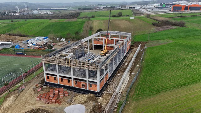 Yapım aşamasında olan modern bina, inşaat sürecinde ve çevresinde yeşil alanlar.